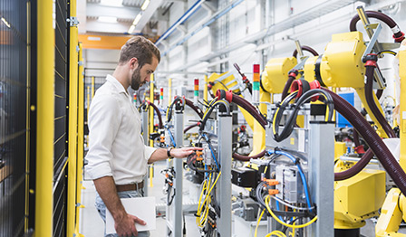 Engineer inspecting automated machinery in a modern manufacturing facility, surrounded by robotic arms and industrial equipment.