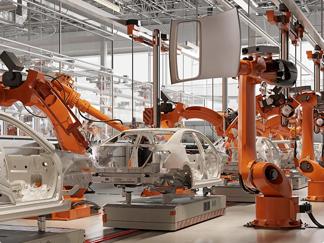 Orange robots welding car frames on an assembly line.