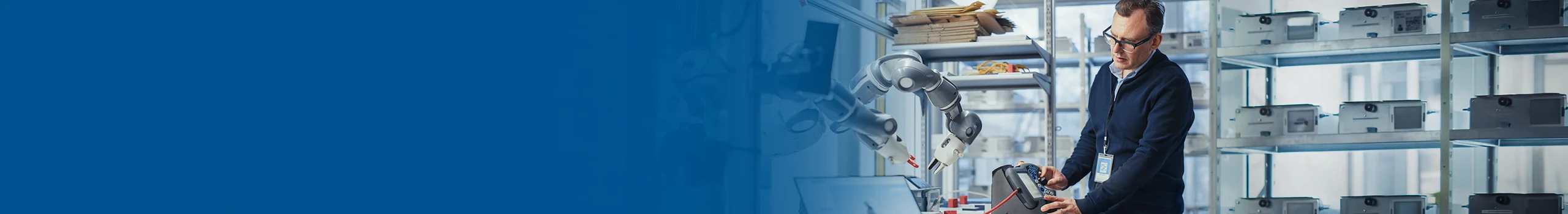 A man in a lab coat operates a control panel near a robotic arm and laptop displaying a 3D model.