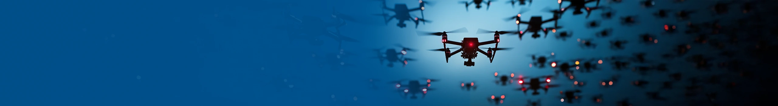 A group of drones with red lights fly in formation against a twilight sky.