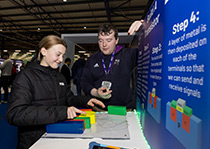 Two individuals engaged in an interactive demonstration involving colorful blocks at an educational exhibit.
