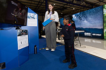 Child engaging with a motion-sensing game at an Analog Devices exhibit, supervised by a staff member