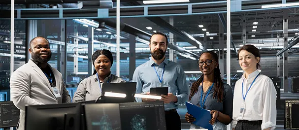 Five diverse IT professionals smiling in a server room.