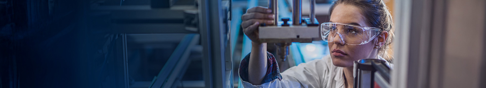 Female engineer in safety glasses focused on adjusting metal equipment.