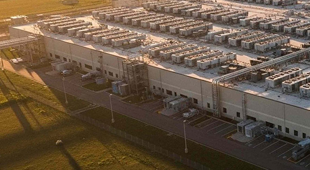 Aerial view of a large data center complex with extensive rooftop cooling units at sunset