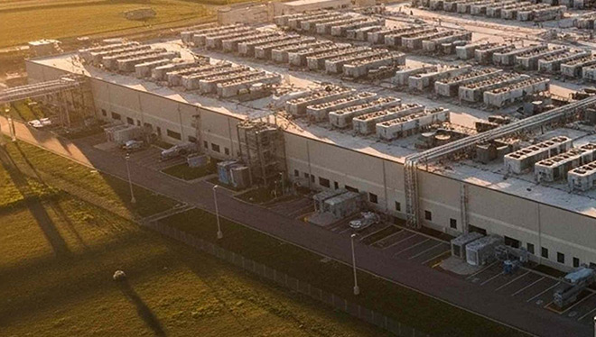 Aerial view of a large data center complex with extensive rooftop cooling units at sunset