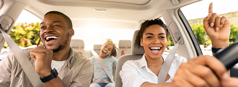 Happy family singing and enjoying a road trip in a car on a sunny day