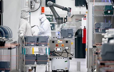 Cleanroom workers and mobile robot with arm in a factory.