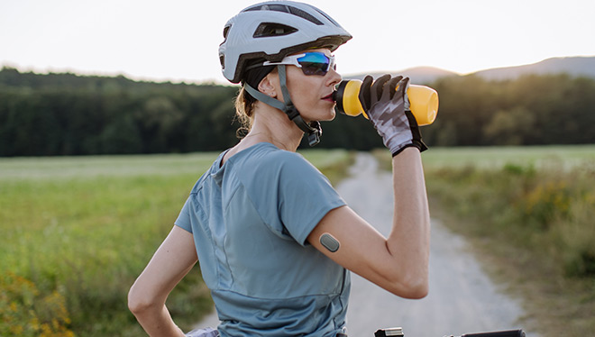 Diabetic cyclist with a continuous glucose monitor on her arm drinking water during her bike tour. 