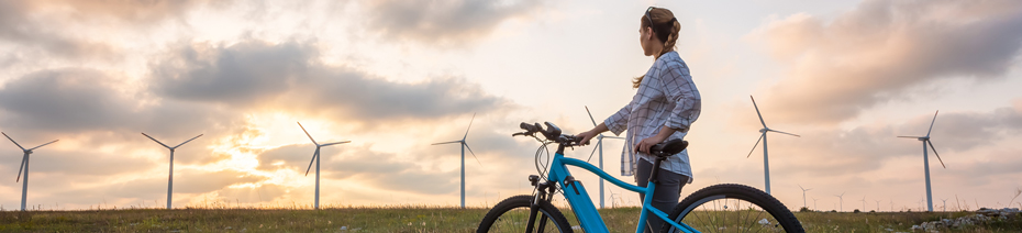 Image shows a woman standing next to an e-bike in front of a wind turbine field