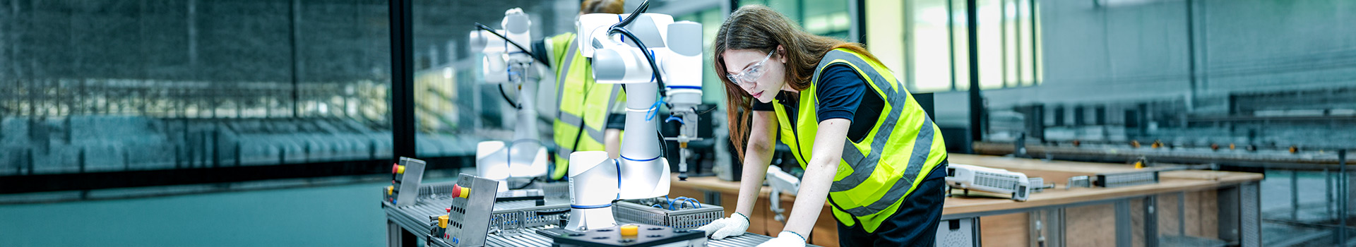 Woman in high-vis vest and glasses working with robotic arms.