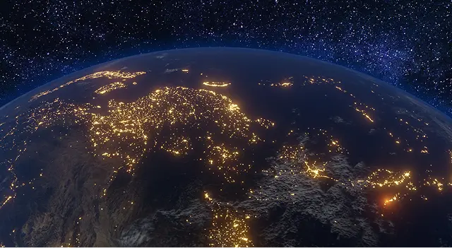 View of Earth from space at night, showing illuminated city lights across Europe and surrounding regions, with a star-filled sky in the background.