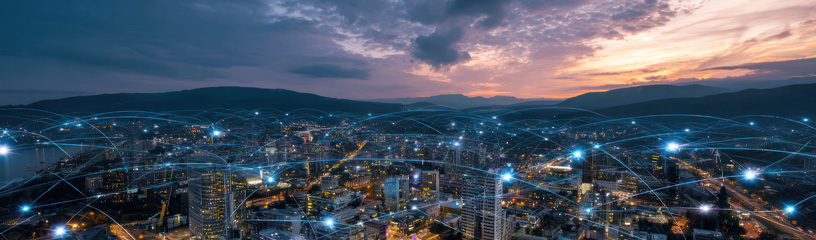 Panoramic city skyline at dusk with illuminated buildings and digital network lines representing wireless connectivity.