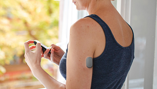 Woman checking glucose levels on smartphone with wearable glucose monitor on arm