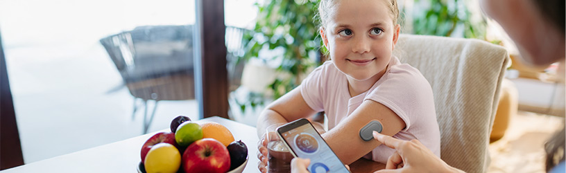 Smiling child with glucose monitor on arm getting blood sugar reading via smartphone