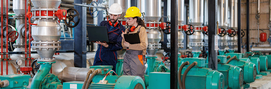 2 engineers having a conversation in a factory surrounded by pumps