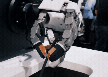 Robotic gripper with articulated fingers grasping a cable, mounted on industrial equipment at a technology demonstration.