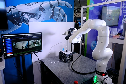 White robotic arm working with blue and black objects, monitor shows feeds.
