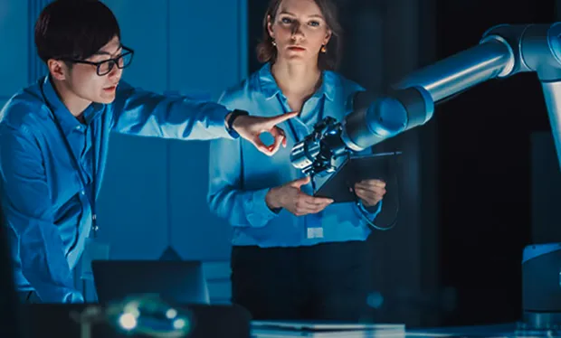 Two engineers collaborate with a robotic arm in a blue-lit lab.