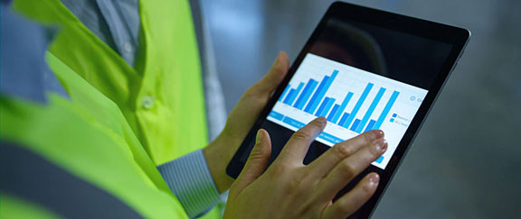 Person in high-visibility vest interacts with tablet showing blue bar graph.