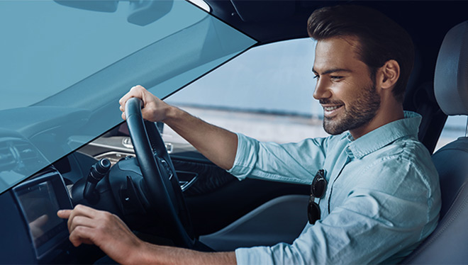 Smiling man driving car, hand on wheel, touching dashboard screen.