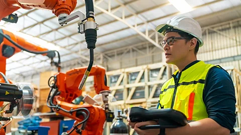 Engineer controls robotic welders in a factory.