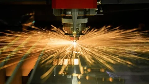 Laser cutting metal with a shower of bright orange sparks.