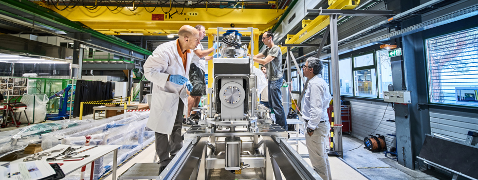 Image displays the inside of a building where several people are working on CERN's mechanical technologies.