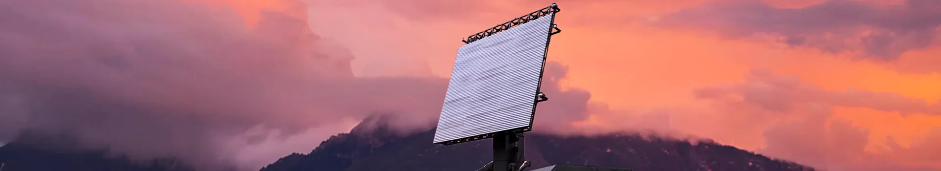 Phased array radar against a vibrant sunset sky with mountains.