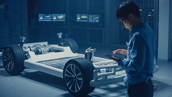 Engineer with tablet inspects EV chassis in a lab.