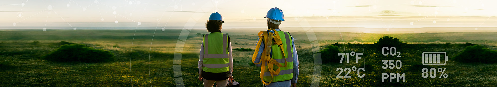 A woman and a man, both installers, standing and looking at a green landscape during sunrise.