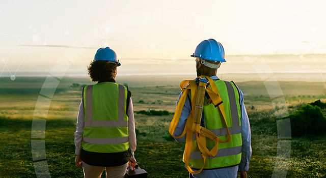 A woman and a man, both installers, standing and looking at a green landscape during sunrise.