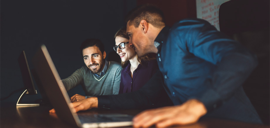 a group of people excitedly disucssing and working together on their laptops