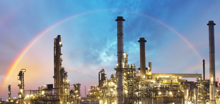 Image shows a gas refinery production plant with bright sky and full specttrum rainbow in the background.