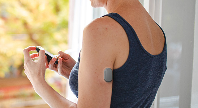 Woman checking glucose levels on smartphone with wearable glucose monitor on arm