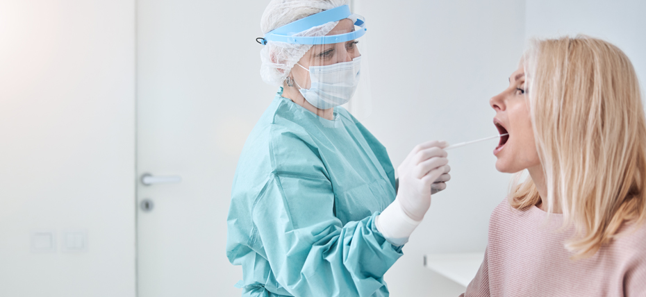 Image shows a female doctor taking a swab sample from a females mouth area to test for viral particles.