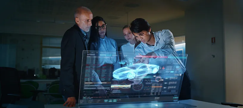 Four people examining a holographic car model on a transparent screen.