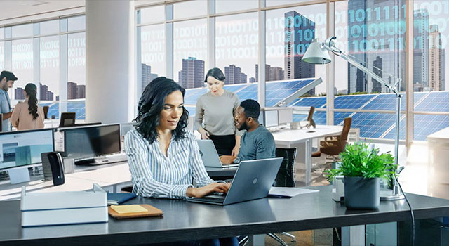 Diverse employees working in a modern office with solar panels outside and a cityscape in the background.