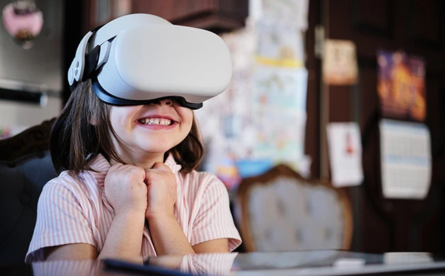 Smiling girl wearing a VR headset, hands clasped in excitement, in a home setting.