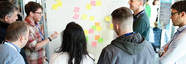 Team discusses whiteboard covered in post it notes