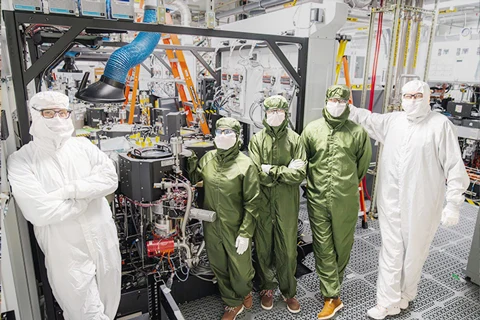 Five scientists in white and green cleanroom suits in a lab.