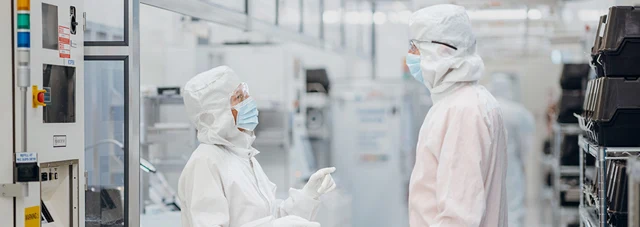 Two people in cleanroom suits talking in a sterile facility.