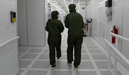 防塵衣を着用して、製造施設のクリーンルームの廊下を歩いている2人の作業者。