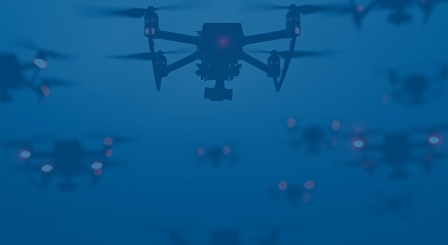 A group of drones with red lights fly in formation against a twilight sky.