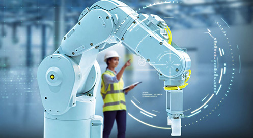 Industrial robotic arm operating in a factory setting with a worker in safety gear interacting in the background.