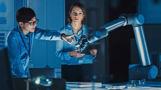 Engineers working with a robotic arm in a blue-lit lab.