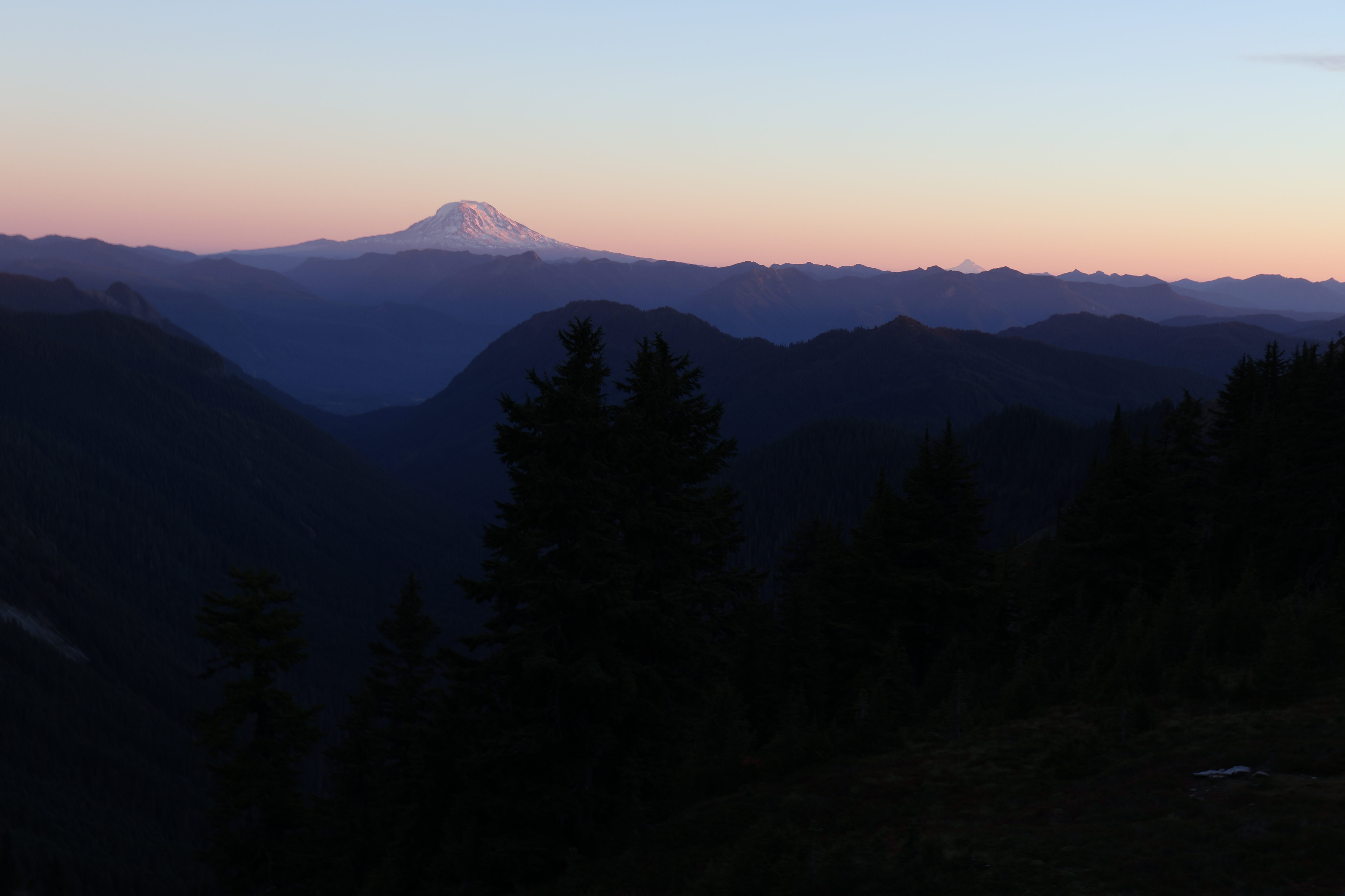 Mount Rainier glowing at sunset above dark, layered mountains.