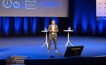 Speaker, Fionn Hurley presents on a large stage, discussing "Intelligent Nervous System Drives A Resilient, Software-defined Vehicle"