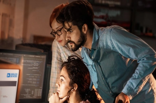 Team of people working around a computer to solve a problem.