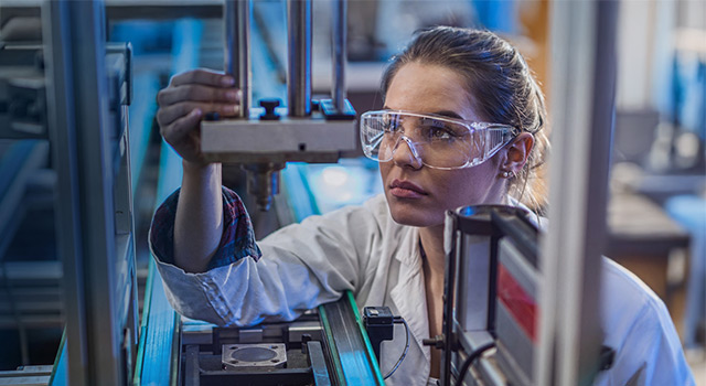 Female engineer in safety glasses focused on adjusting metal equipment.